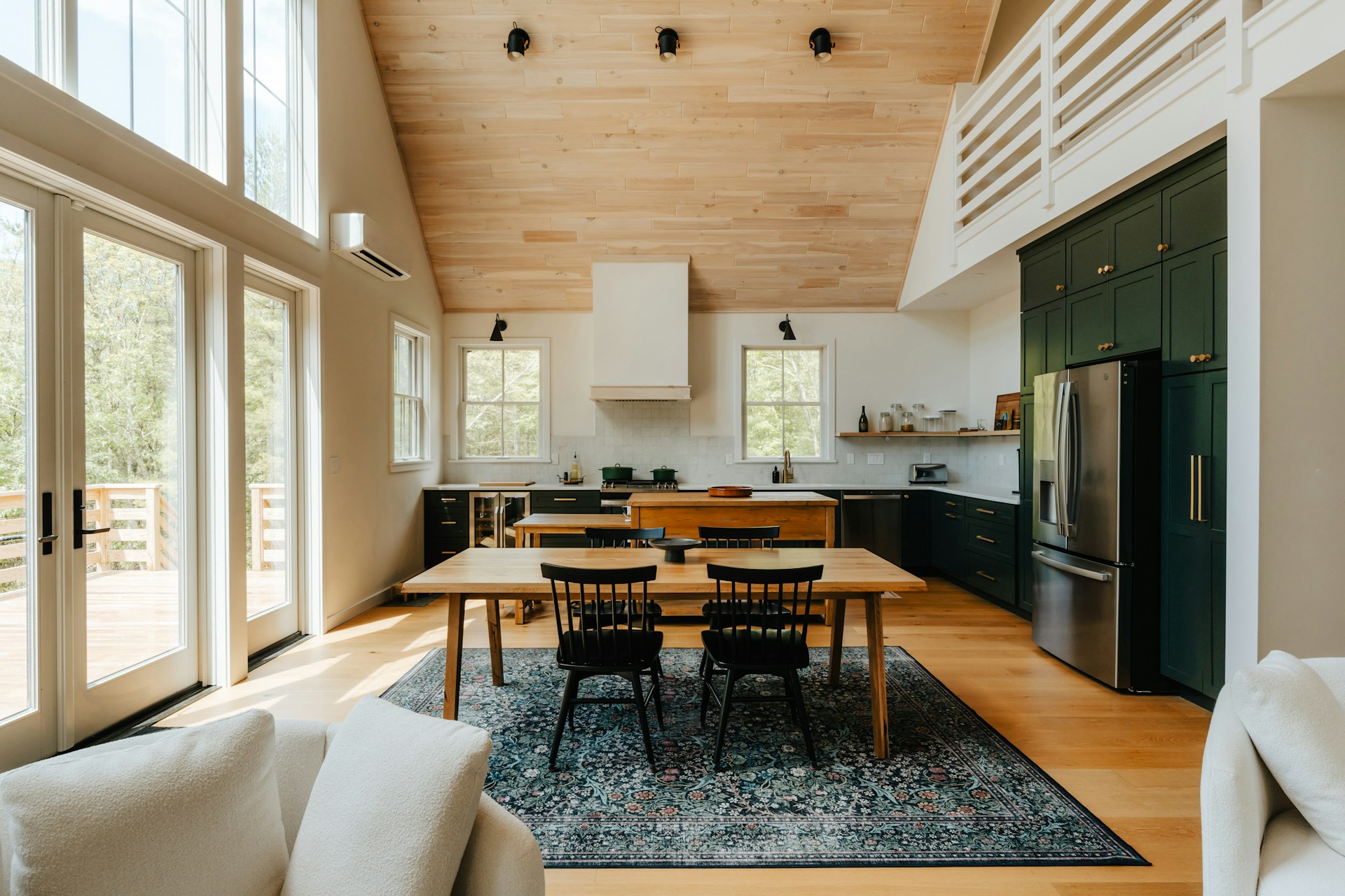 The dining room is a welcoming space with a central 8x12 vintage rug. The rug is a blend of dark and vibrant colours, and the room's aesthetic is enhanced by the abundance of daylight and the positioning of the kitchen furniture. The image depicts a dining room and kitchen where the ambience is distinctly cosy. This demonstrates that the carpet not only enhances the visual appeal of the room, but also enriches the experience of being in the room.