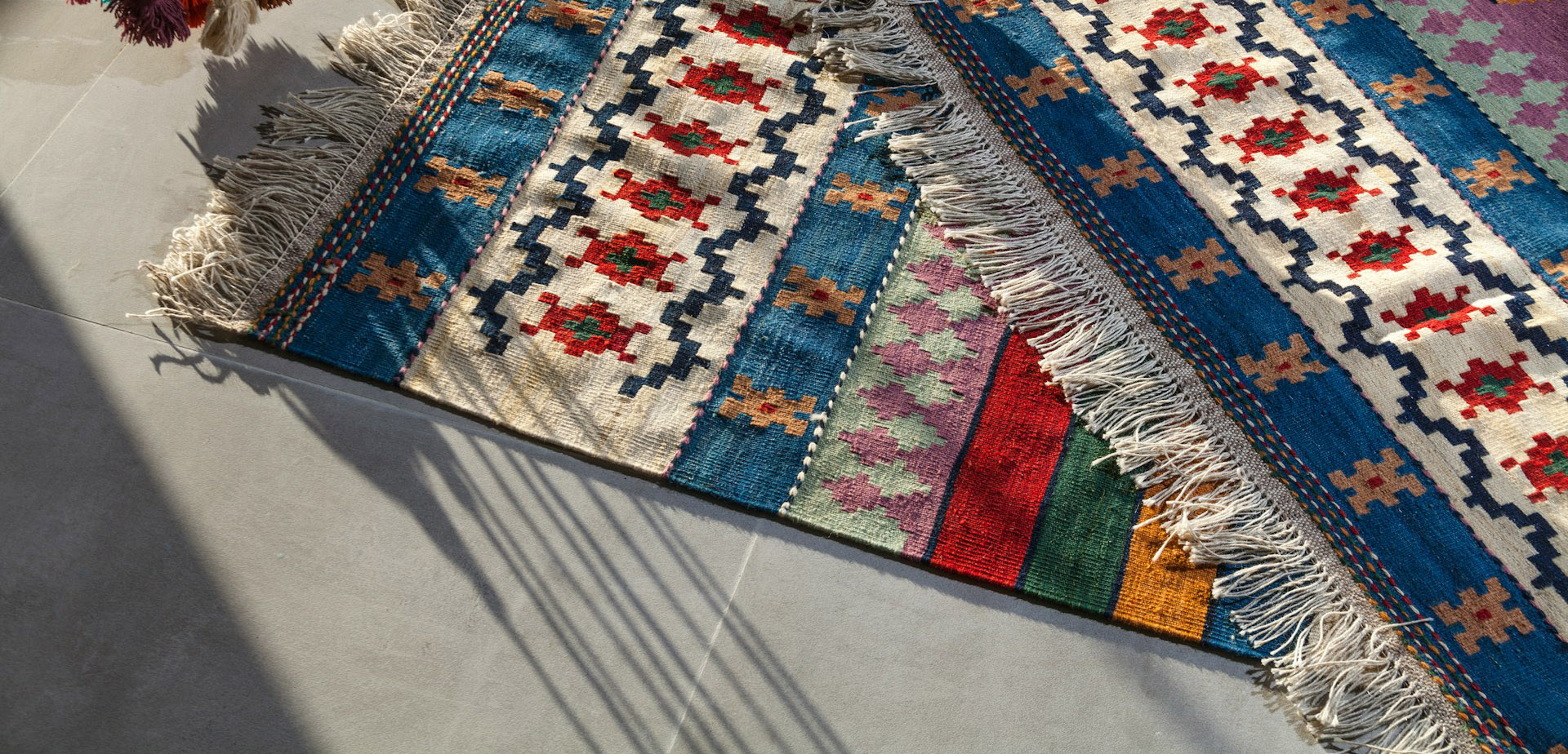 A close-up view of two traditional Turkish kilims with striped and diamond motifs in vibrant shades of blue, red, and white, showcasing their texture and fringed edges
