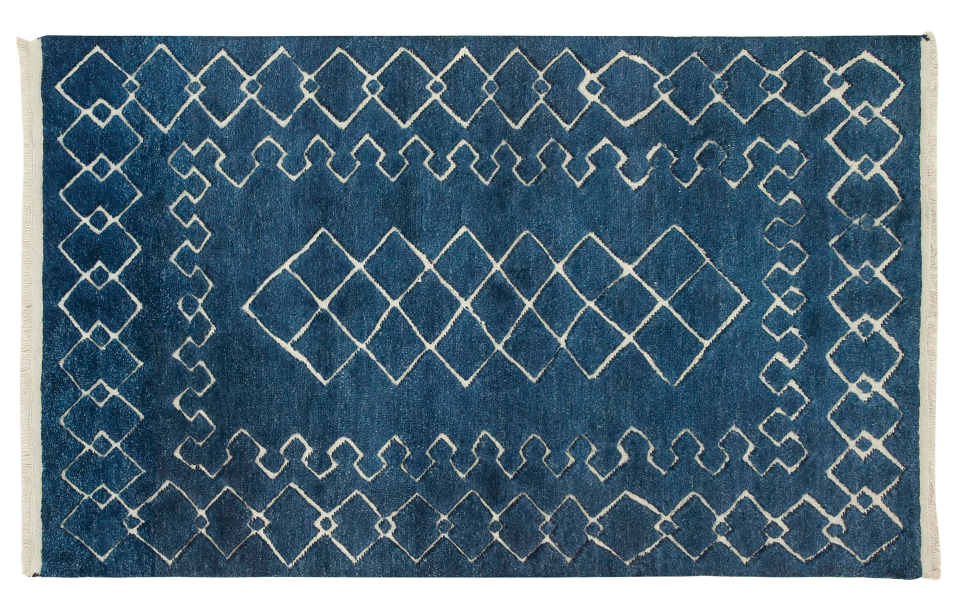 An old Moroccan carpet with blue and white geometric design. A hand-woven carpet with a dark blue background and intricate white geometric patterns.