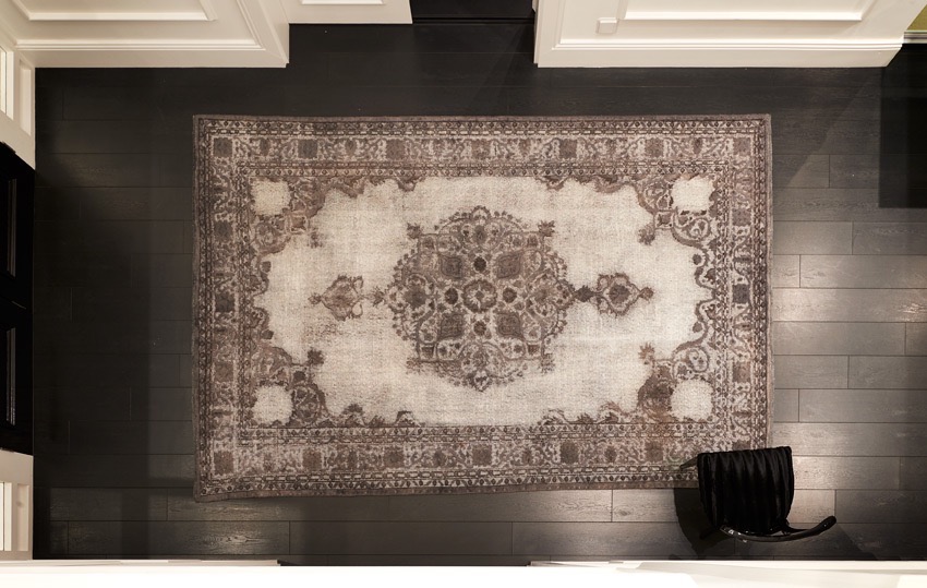 A top-down view of an elegant white room featuring dark wooden parquet flooring. The focal point is a vintage Turkish handwoven rug on the floor, showcasing its intricate design and fine craftsmanship, which add a touch of sophistication to the space