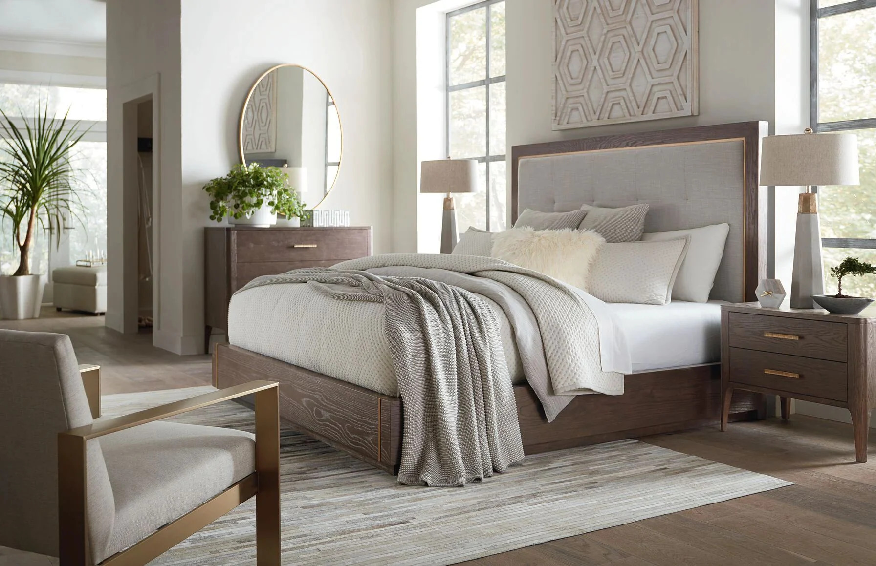 A stylish bedroom featuring a large queen-sized bed with a light gray and white abstract area rug extending beneath it, perfectly illustrating ideal rug placement and size for a bedroom, with a modern mirrored dresser and two nightstands.