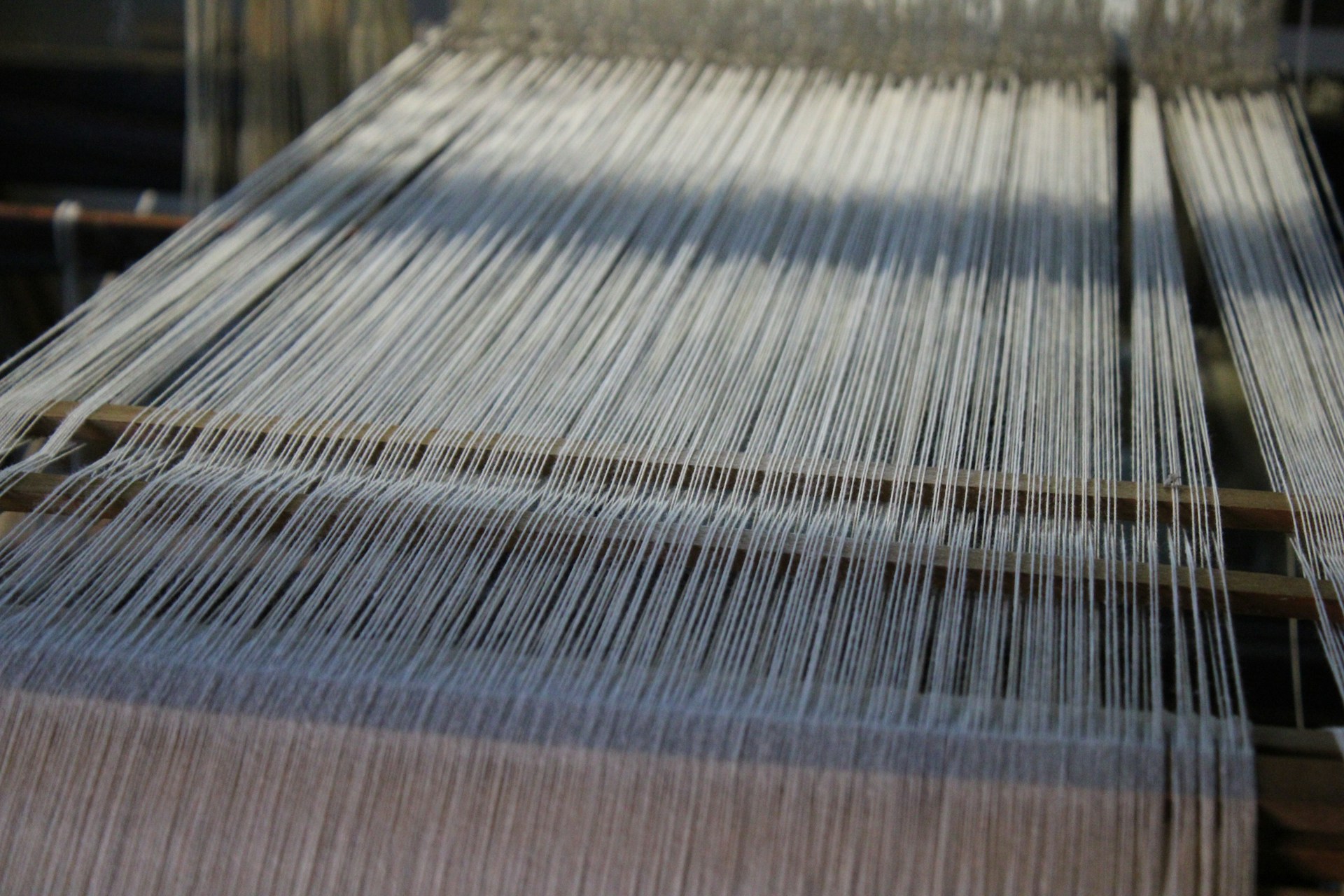 A large Turkish rug is being crafted on a traditional loom. The photo captures the loom itself and the intricate warp threads used in the weaving process, showcasing the detailed craftsmanship involved