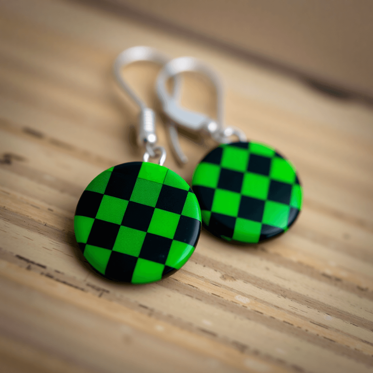 Close-up of handmade earrings with green and black checkered patterns on a wooden background, inspired by anime cosplay fashion.