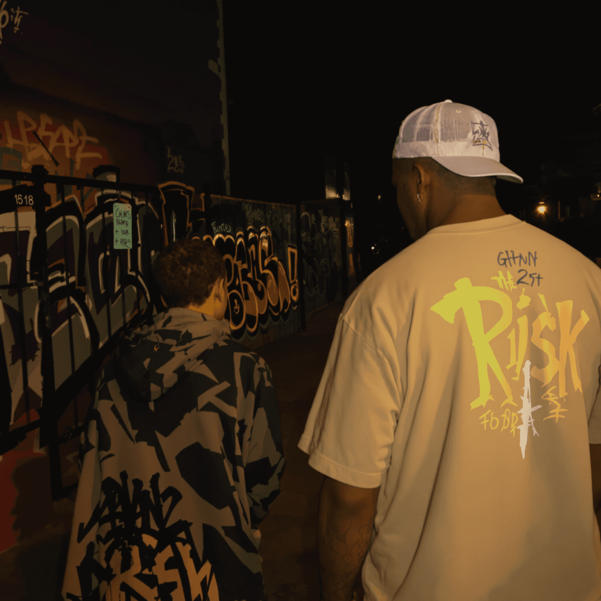 A concerned parent watches a teenager in urban clothing on a graffiti-covered street at dusk, with warm light on the parent symbolizing hope and vigilance.
