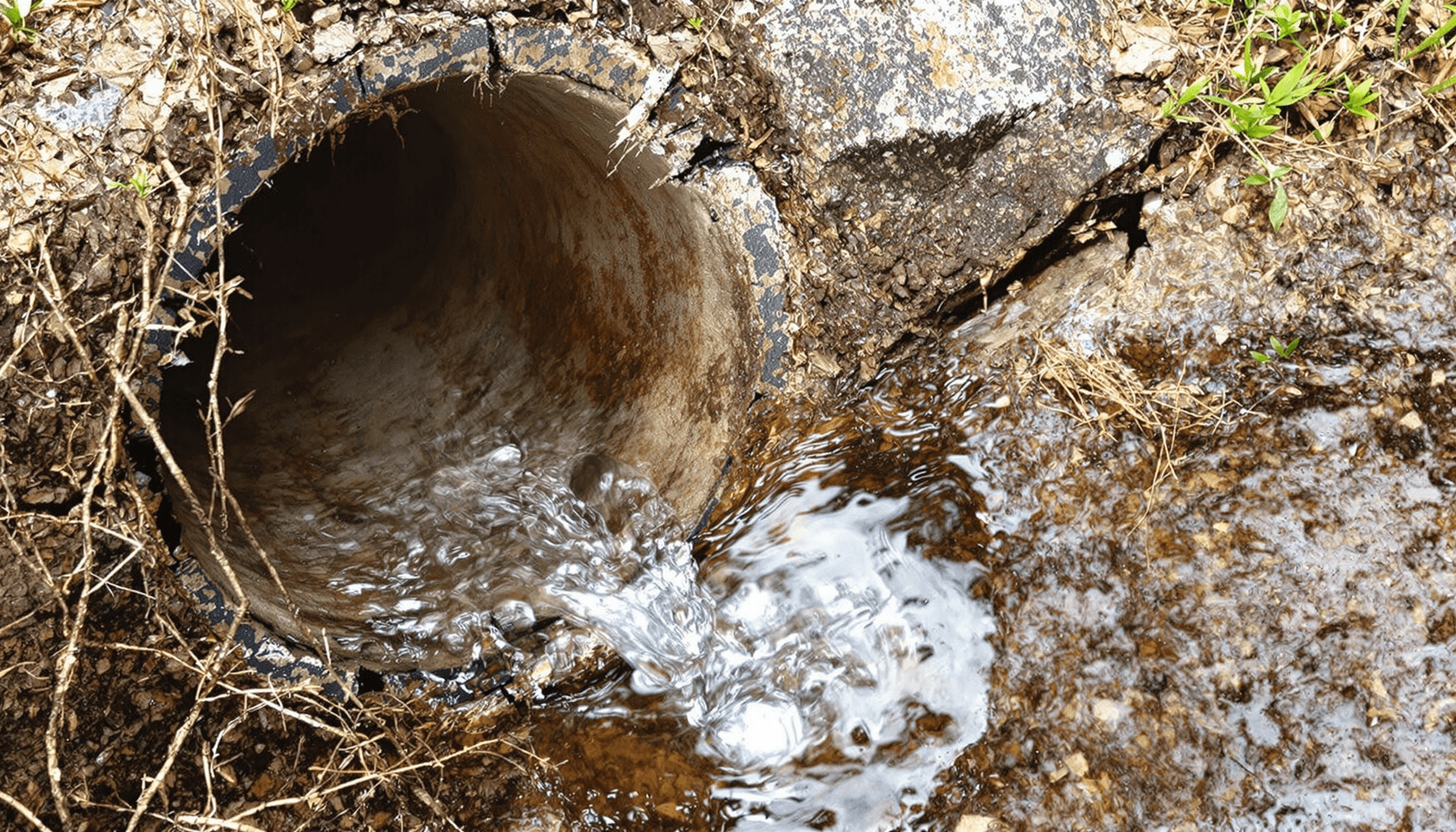 Sewer Line Repair Near Me – Fast, Affordable Service 2025 3 Close-up of a cracked underground sewer pipe leaking water, surrounded by soil and roots, illustrating sewer line damage.