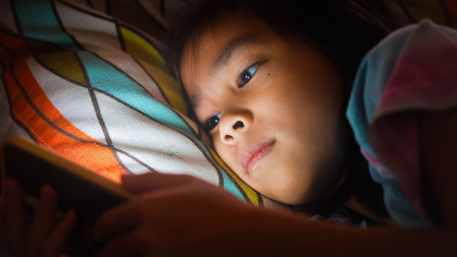 enfant asiatique allongé sur son lit qui regarde son téléphone avec lumière bleue