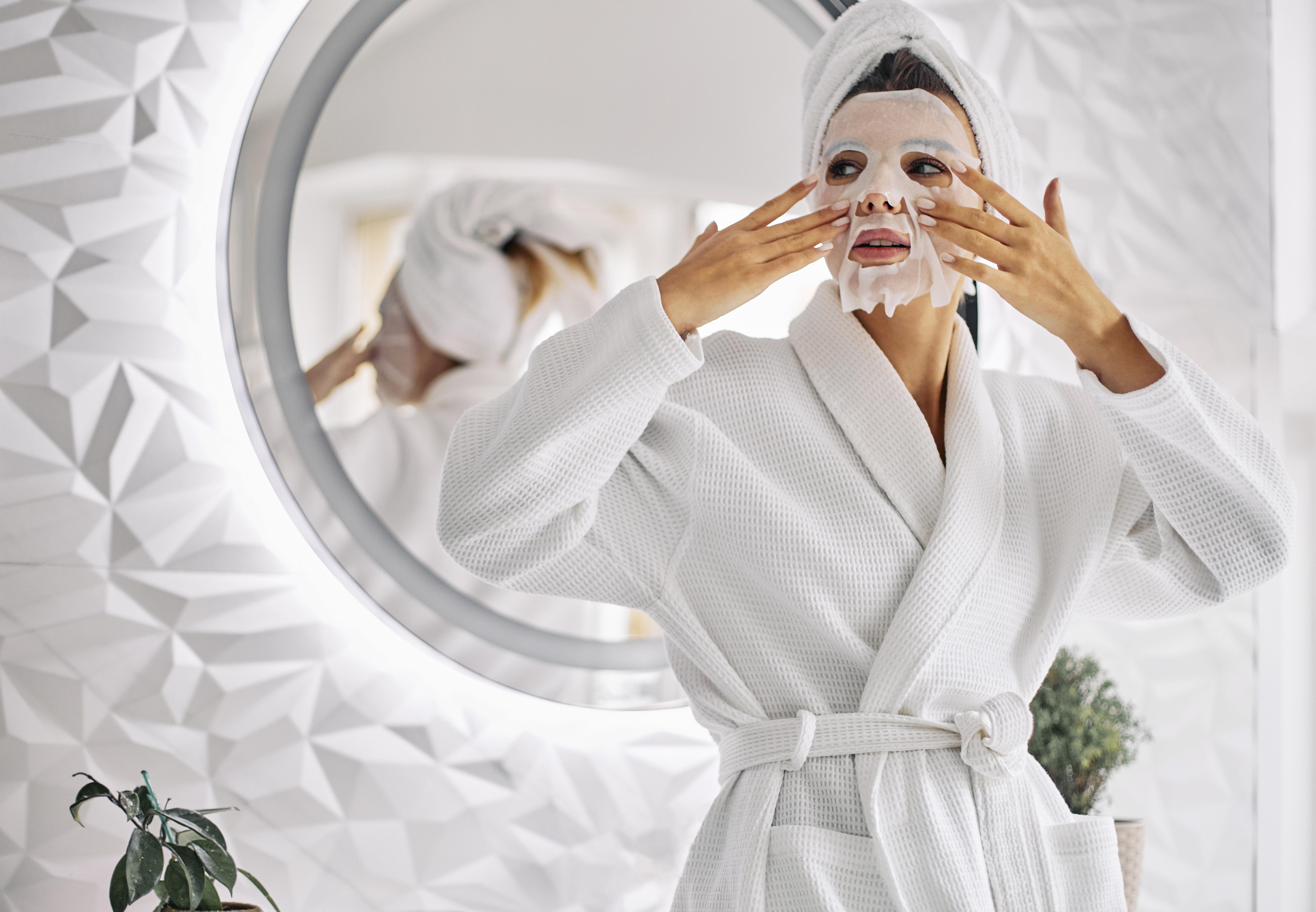 Femme en peignoir qui applique un masque en tissus et qui fait sa skincare routine