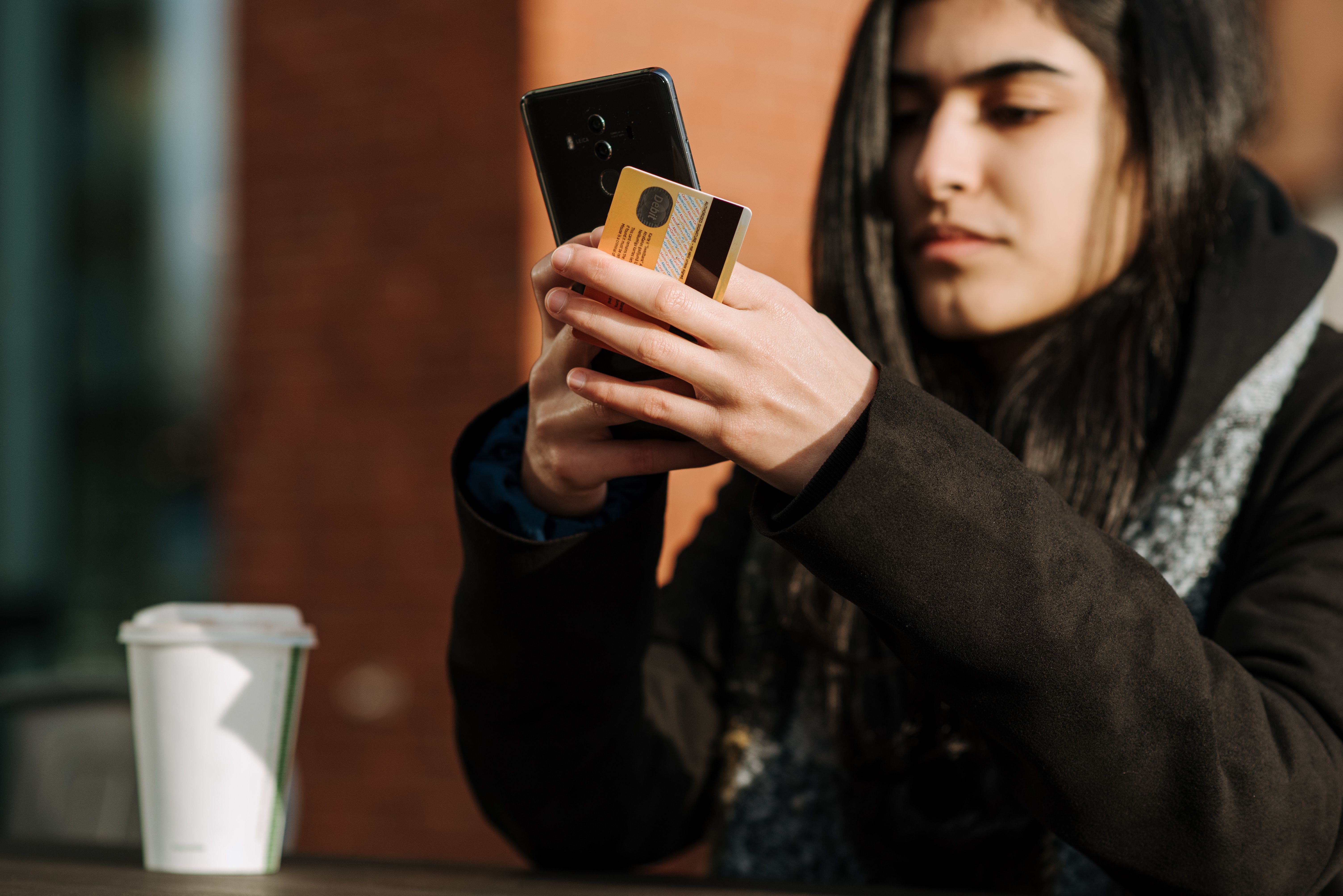 Woman checking her phone while holding a credit card in a café