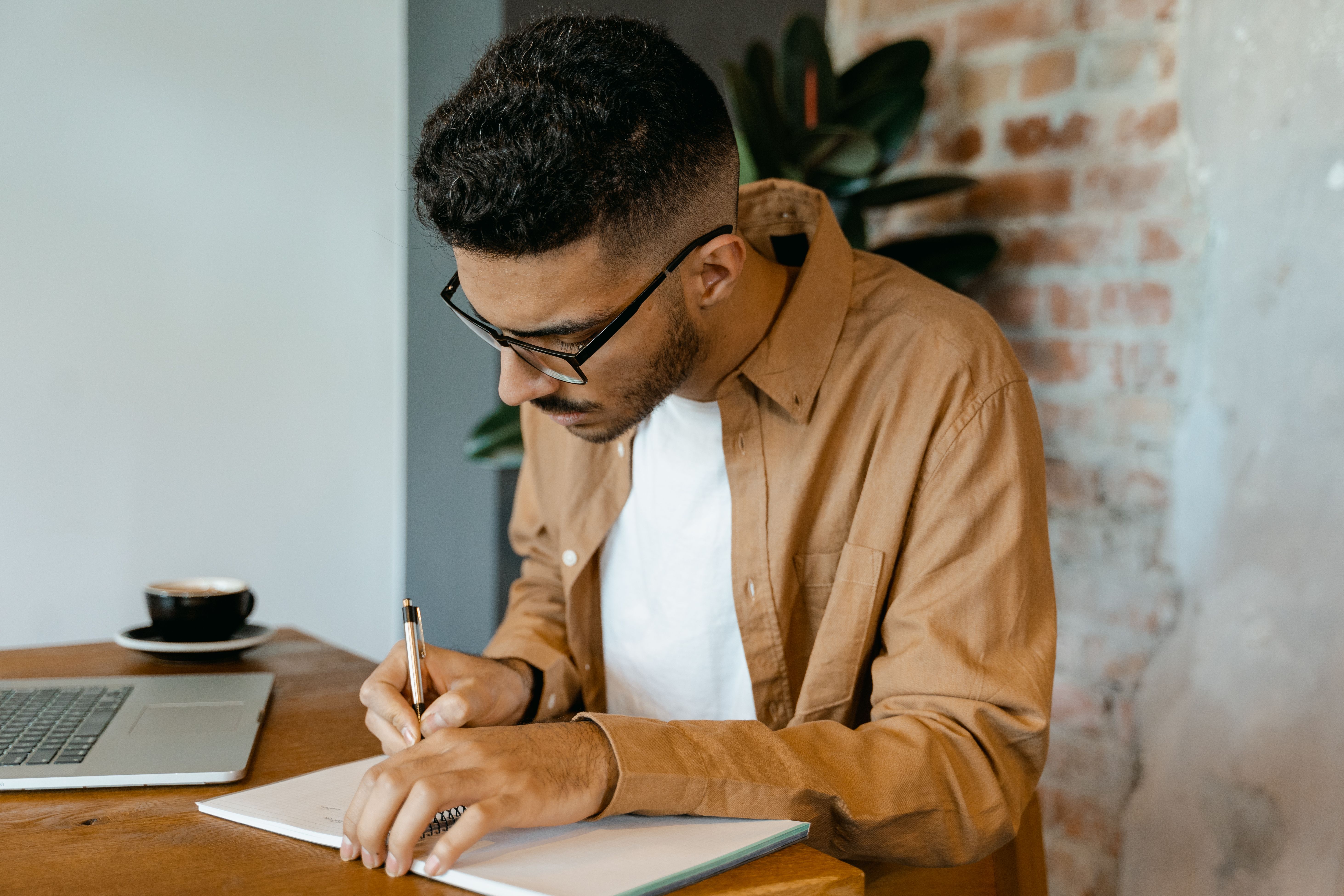 Man writing monthly budget figures beside a laptop and coffee at a desk