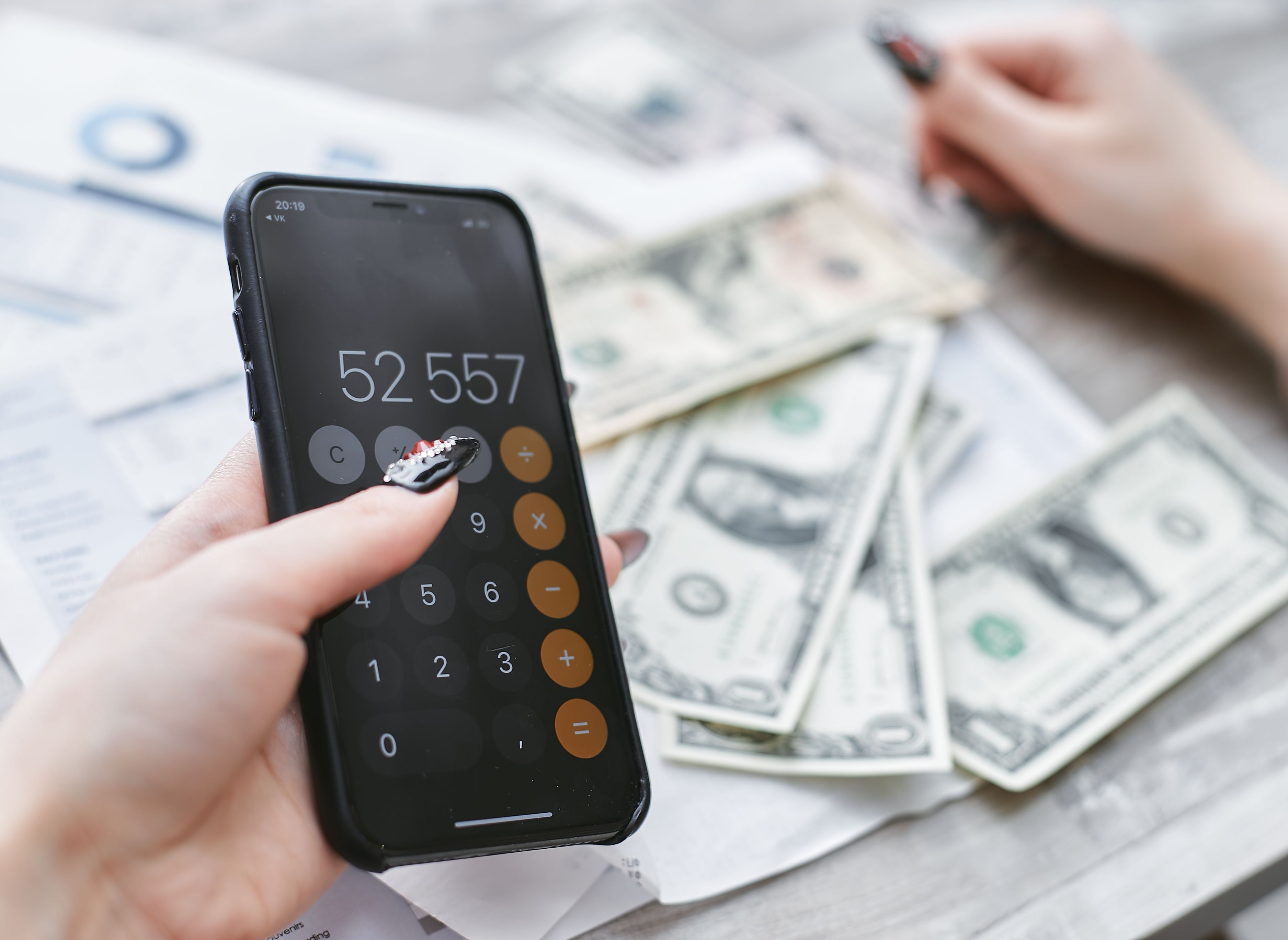 Person calculating expenses on a smartphone beside cash and financial paperwork
