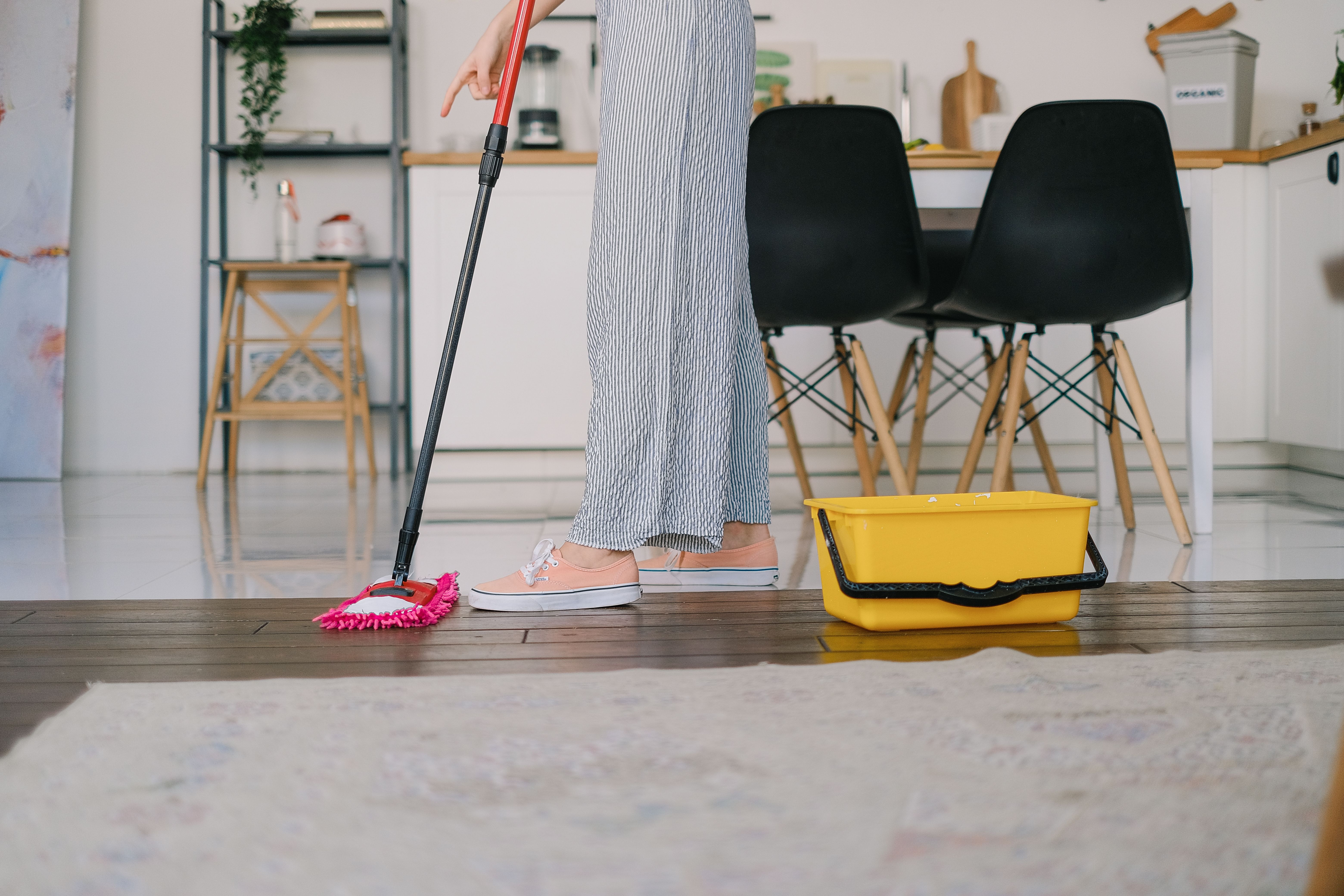 Person mopping the floor beside a bucket in a bright kitchen