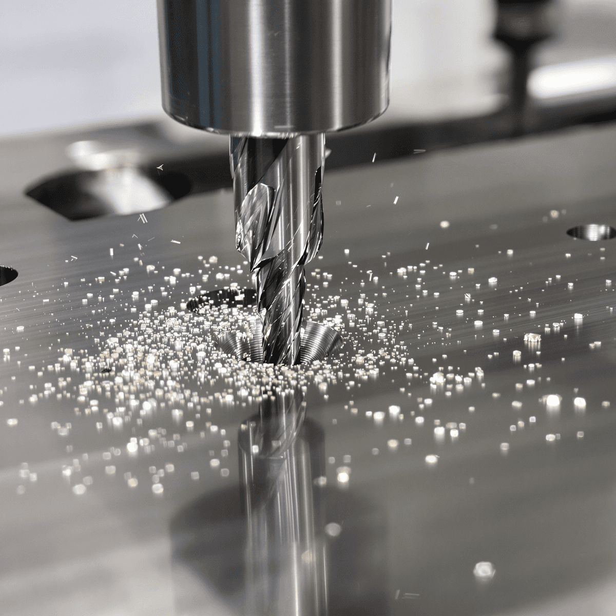 Close-up of a precision reamer cutting into shiny metal, showing fine shavings and smooth polished hole surfaces in a high-tech machining workshop.
