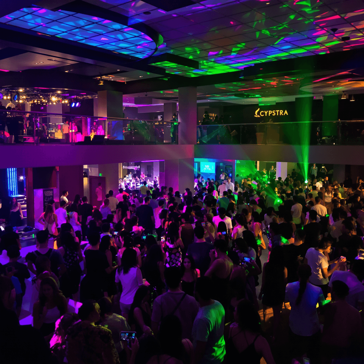 Canlı Akdeniz gece kulübü, renkli ışıklar, modern iç mekanlar ve dans eden, müziğin tadını çıkaran canlı bir kalabalıkla enerjik bir gece hayatı atmosferini yansıtıyor.